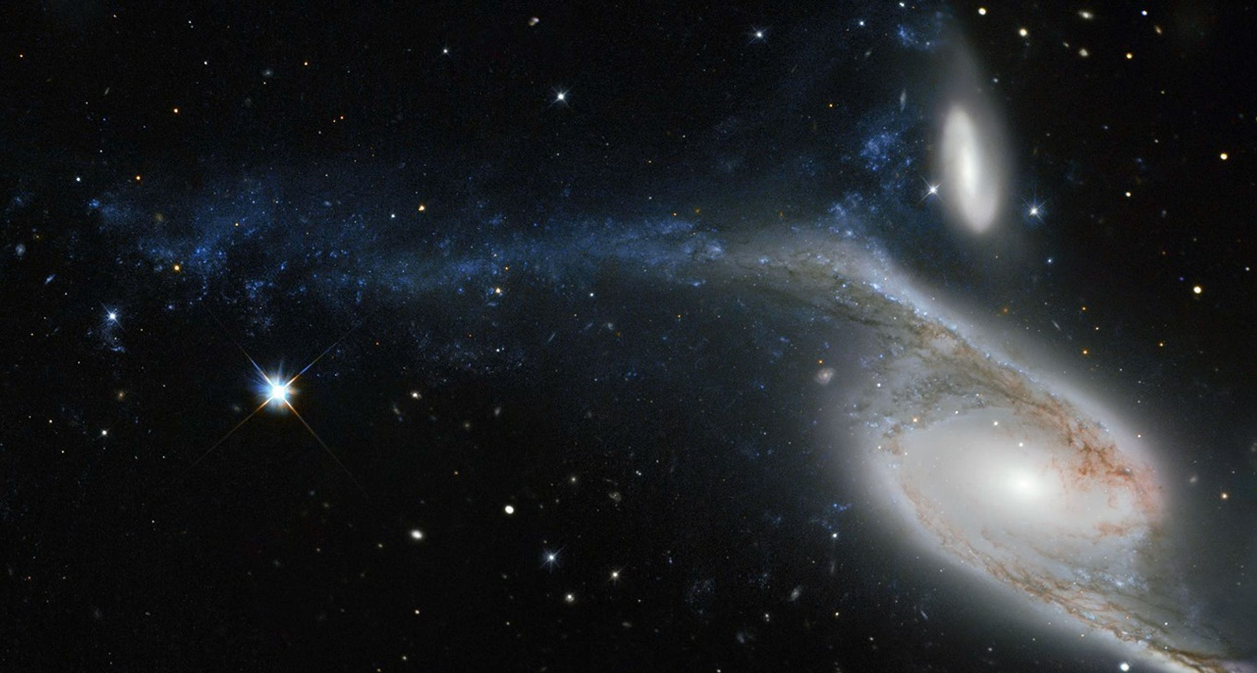 One small spiral galaxy and one large one on the right side of the image, stretched to the left across the field of stars